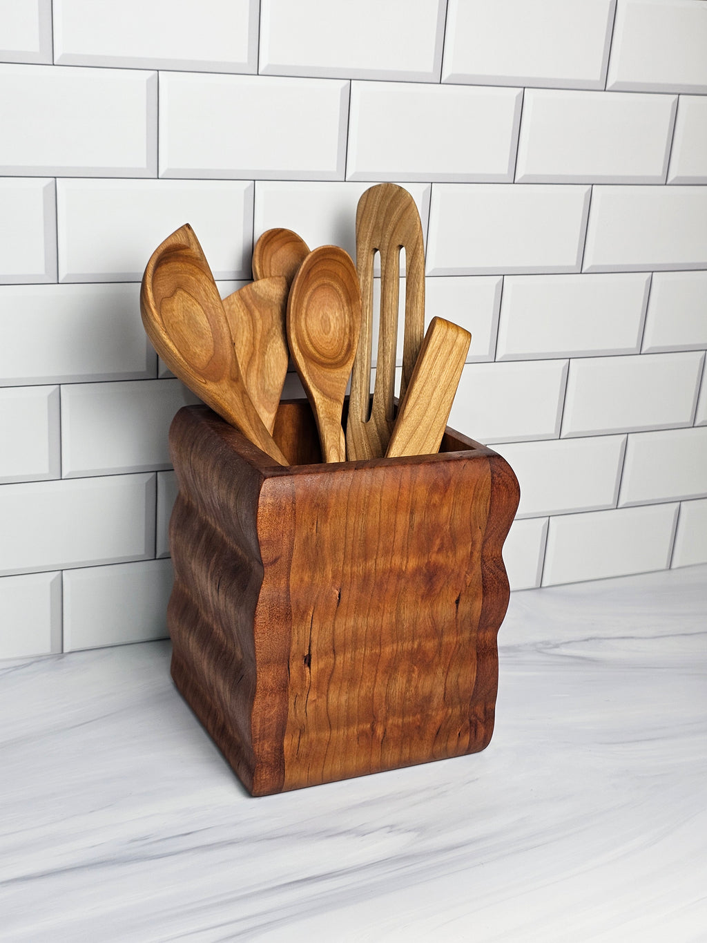 Set of wooden spoons in a wooden holder on a white tiled surface