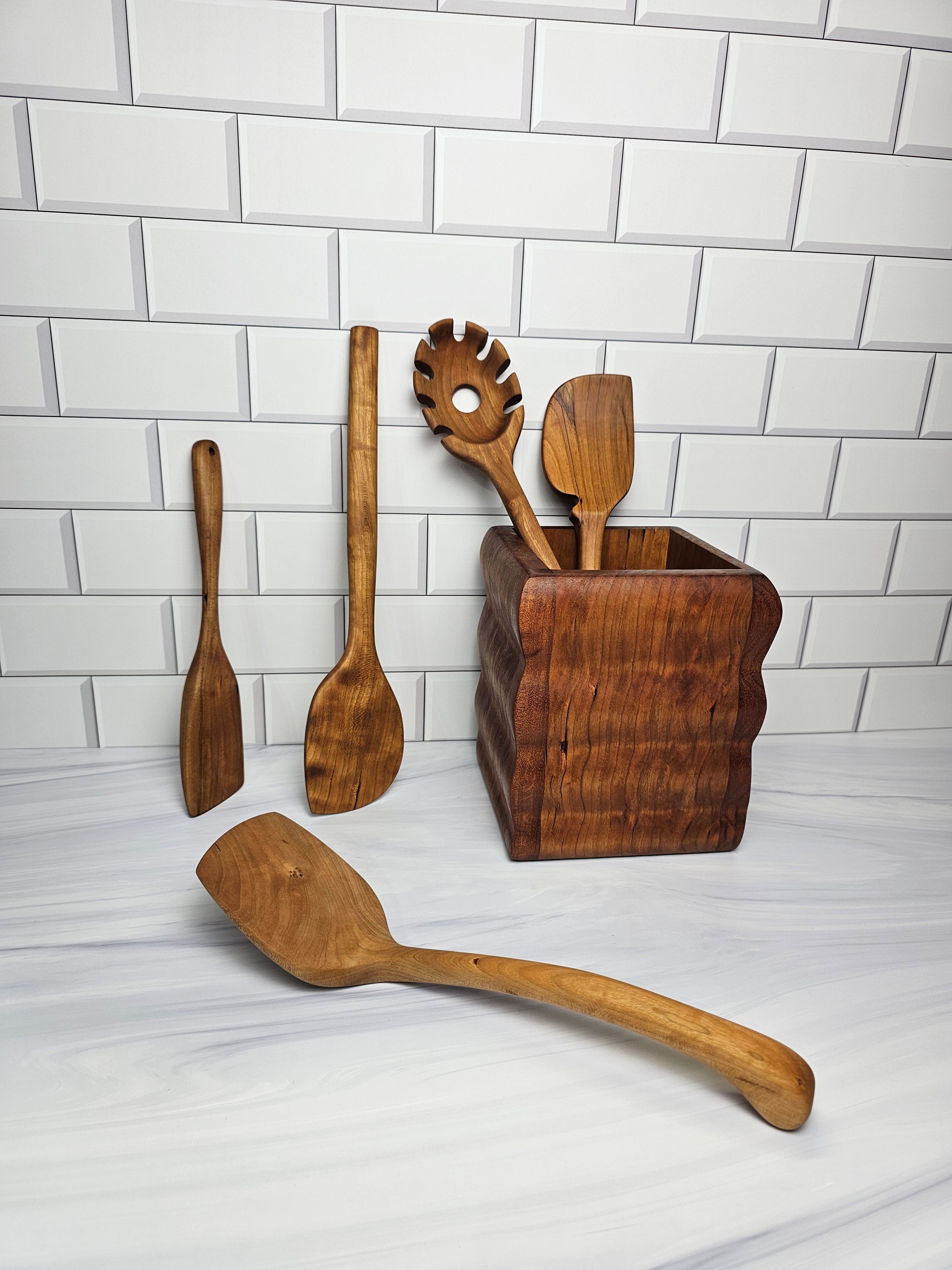 Set of wooden kitchen utensils including a spaghetti spoon and spatulas on a white tiled background